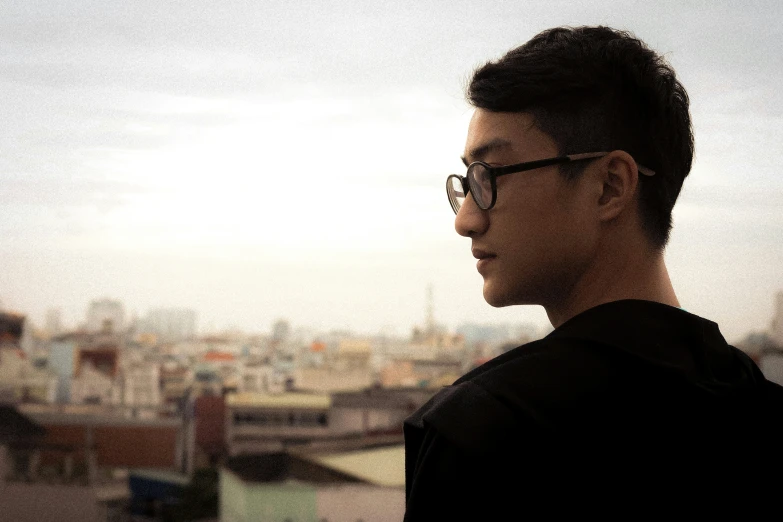 a man with black glasses is standing in front of the city