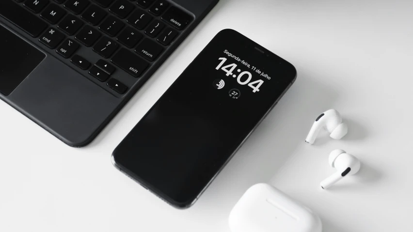 an earphone and a black phone sit beside a keyboard