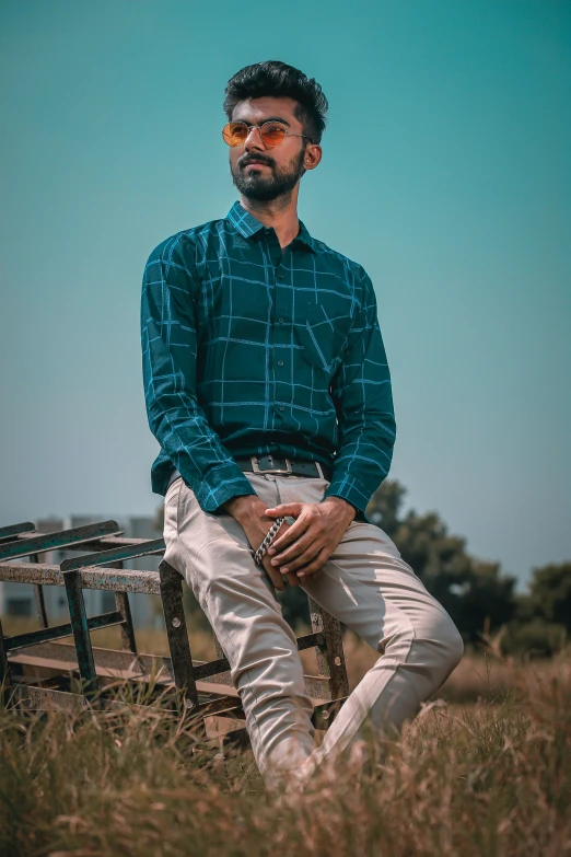 an indian man poses in a field of grass while sitting on a park bench