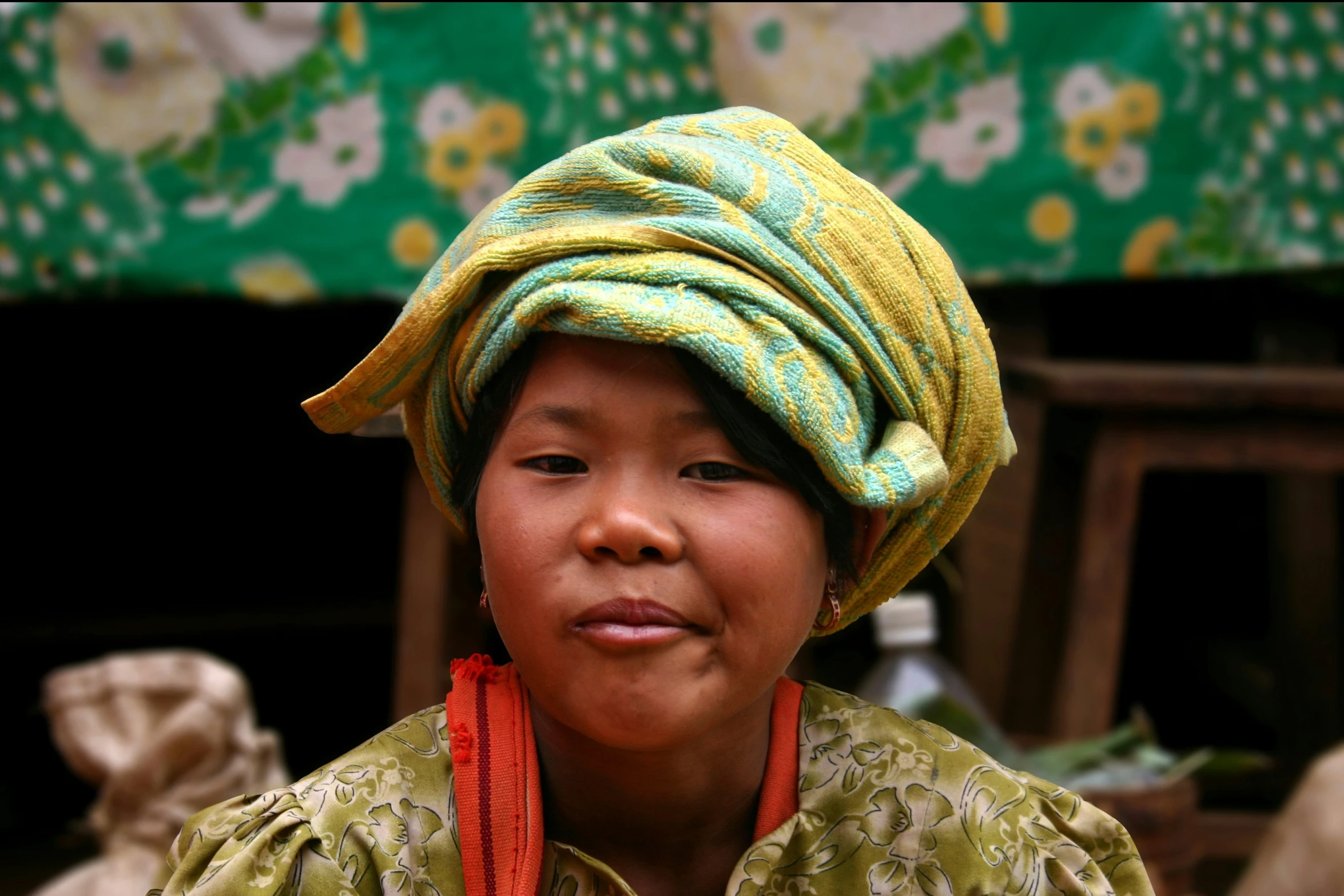 a young child wearing a colorful hat standing next to green and yellow patterned umbrella