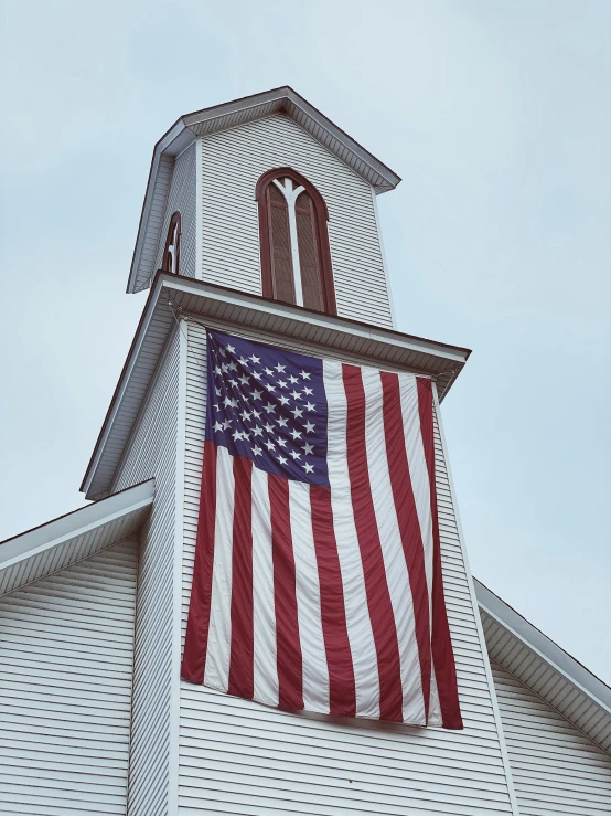 an american flag in the shape of a cross on top of a white building