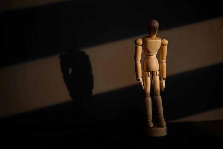 a wooden man that is standing in the shadows