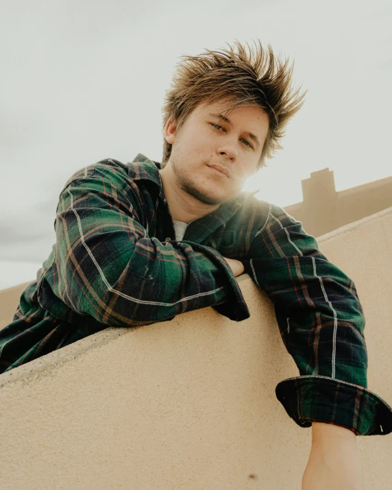 a young man sits on a wall, arms folded