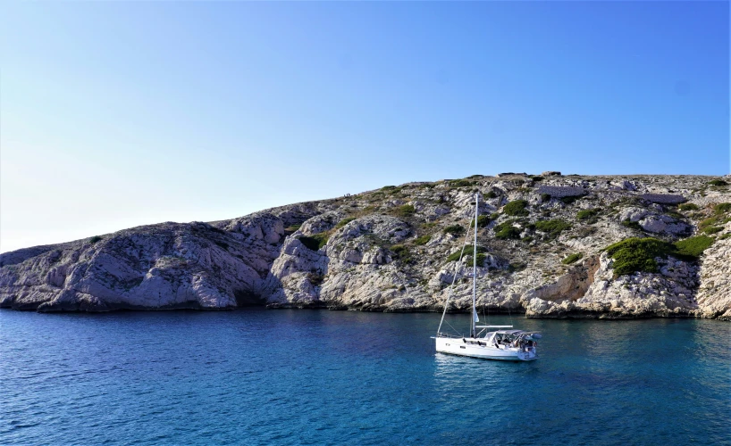 a boat sailing in the blue water next to a rocky hill