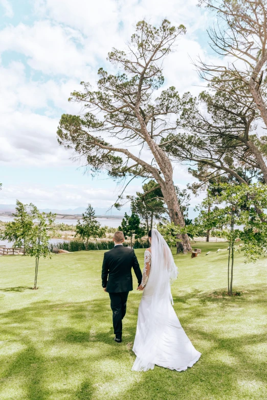 a bride and groom walking through the grass on their wedding day