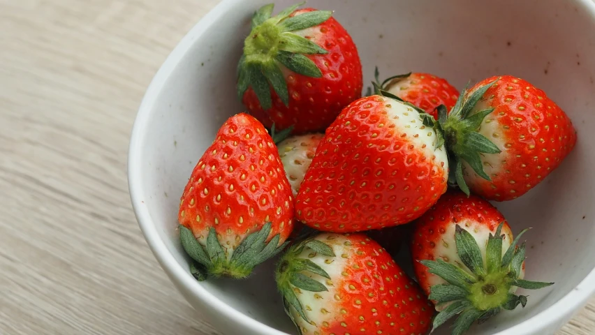 a white bowl full of strawberries on top of a wooden table