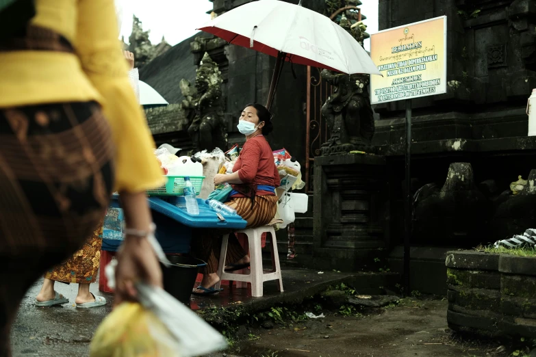 a woman holding a plastic bag sitting at a table with an umbrella