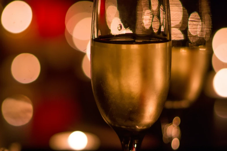 two champagne flutes in a dark room, with blurred lights behind them