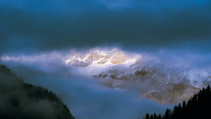 clouds hovers over a snow - covered mountain at dusk