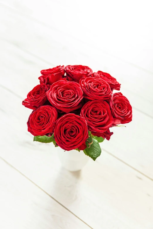 a white vase with a bunch of red roses