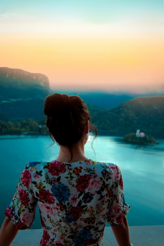 a girl stands on a hill overlooking water at sunset