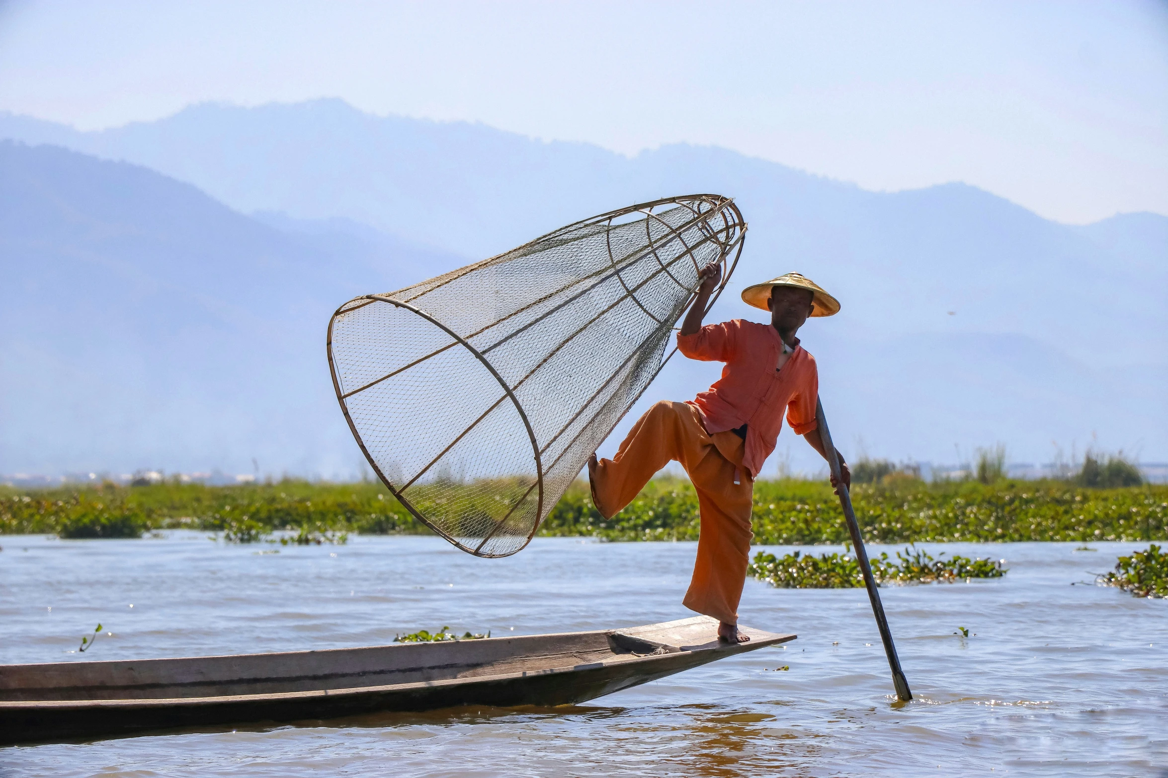 a man stands on a canoe while fishing with his cane