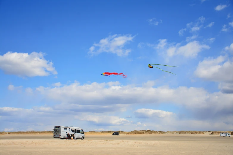 people flying kites on a beach near a vehicle