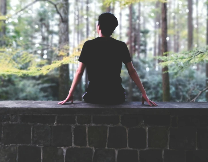 woman sitting on wall looking up at trees