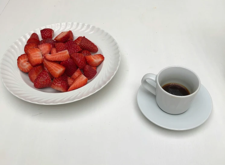 a cup of coffee next to a plate of strawberries