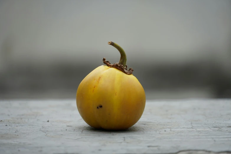 an odd looking yellow apple sits on a gray surface