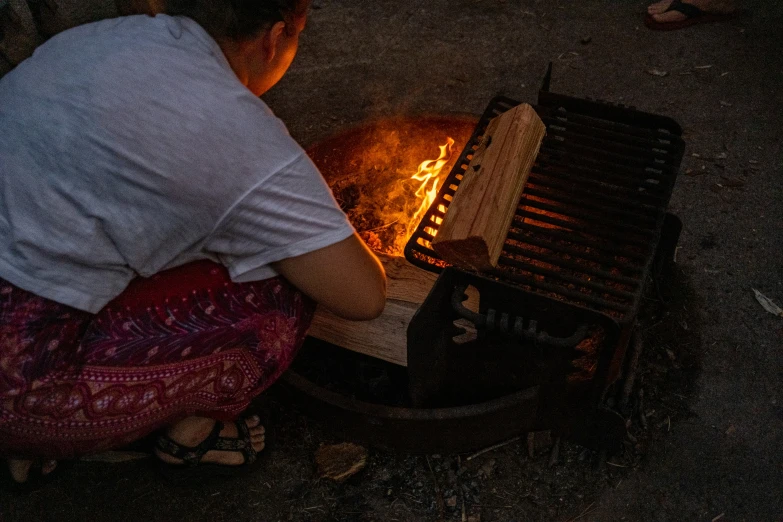 a woman squatting over a cooking pan filled with food