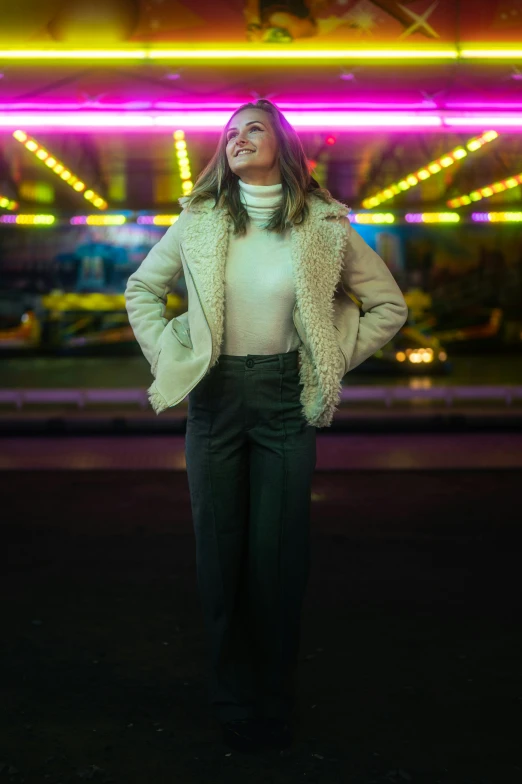 a woman standing next to a neon sign with her arms folded