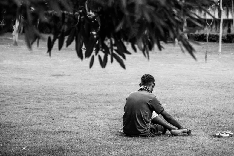 the boy is sitting down on the grass looking at the frisbee