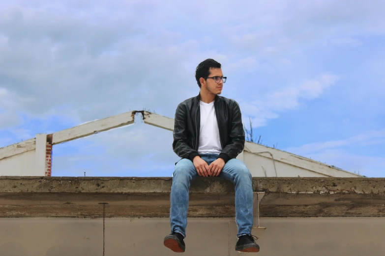 a man in glasses sits on a concrete wall