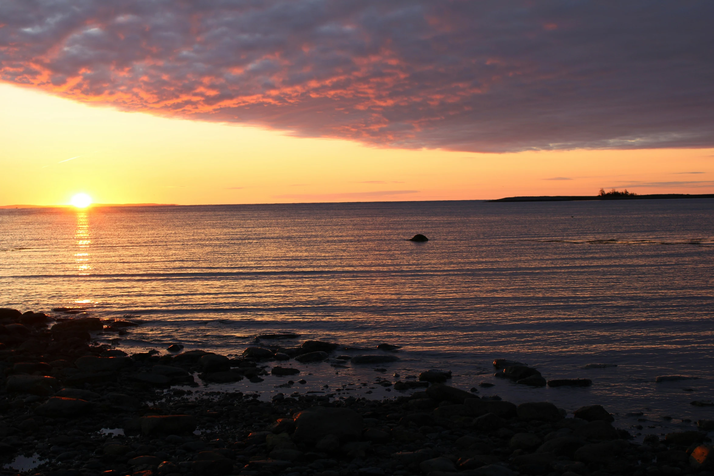 the sun sets over an ocean with rocks and a boat in it