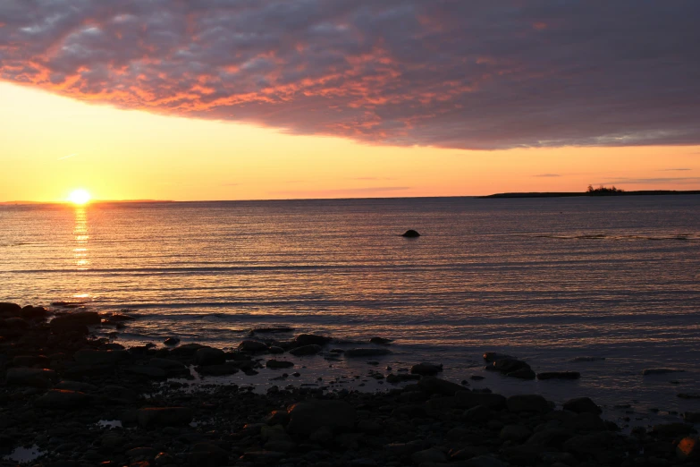 the sun sets over an ocean with rocks and a boat in it