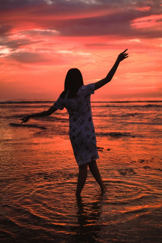 girl wading in the ocean at sunset with arms spread out