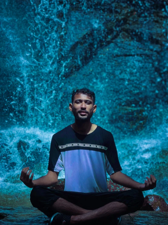 a man sitting in a meditation position in front of a waterfall