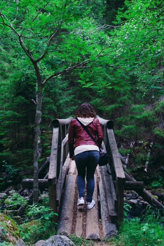 a woman is walking across a wooden bridge in the woods