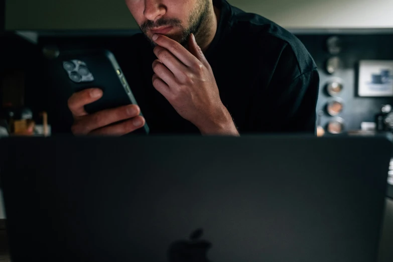 a man looks at his cell phone while working on a computer