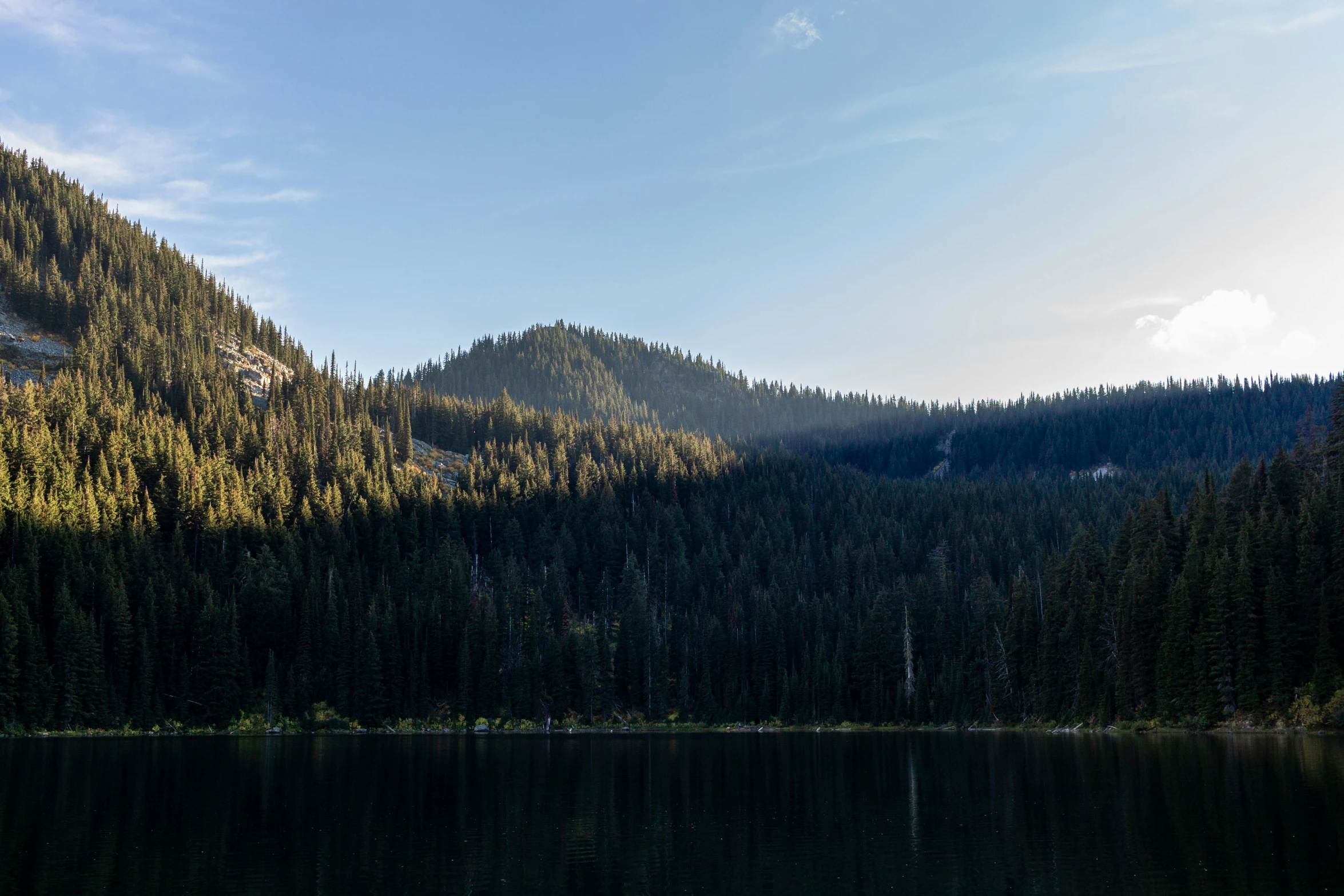 mountains covered in green foliage stand behind a calm lake