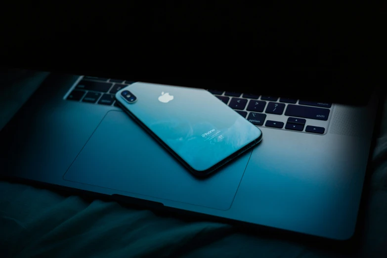 an iphone sits atop the laptop on a blanket