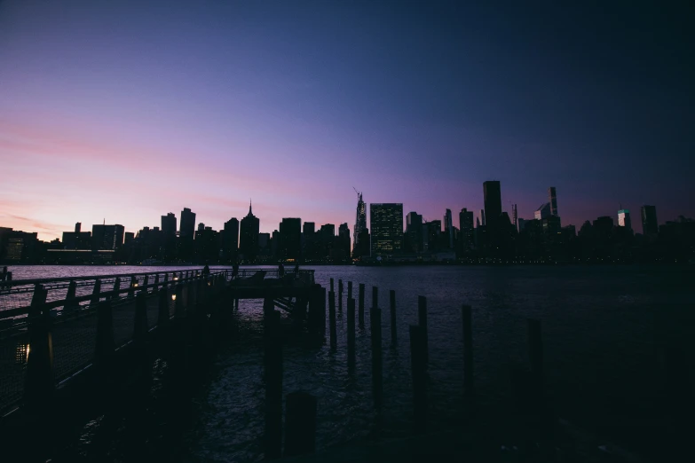 the silhouette of the city buildings in the distance with water around them at dusk