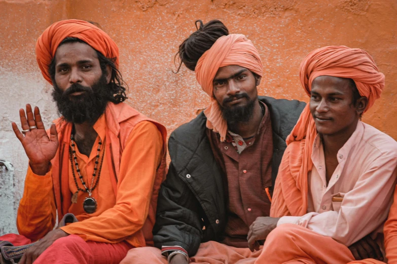 three men sitting on the ground with one man in orange clothes and the other man in grey