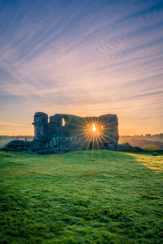 an old ruin sitting in the middle of a field at sunrise