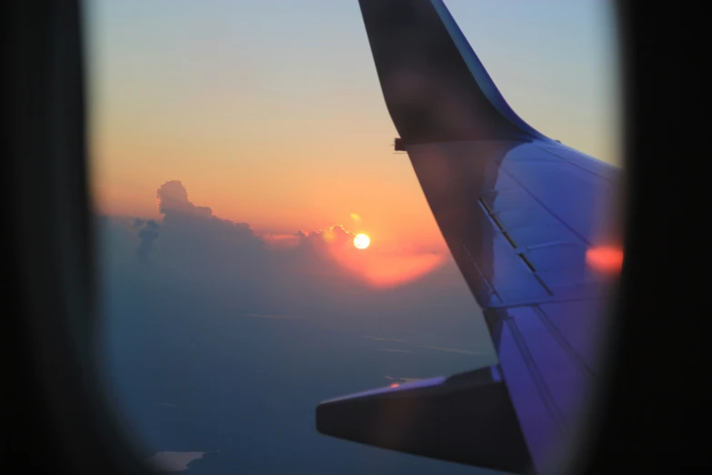 an airplane wing with the sun going down over clouds