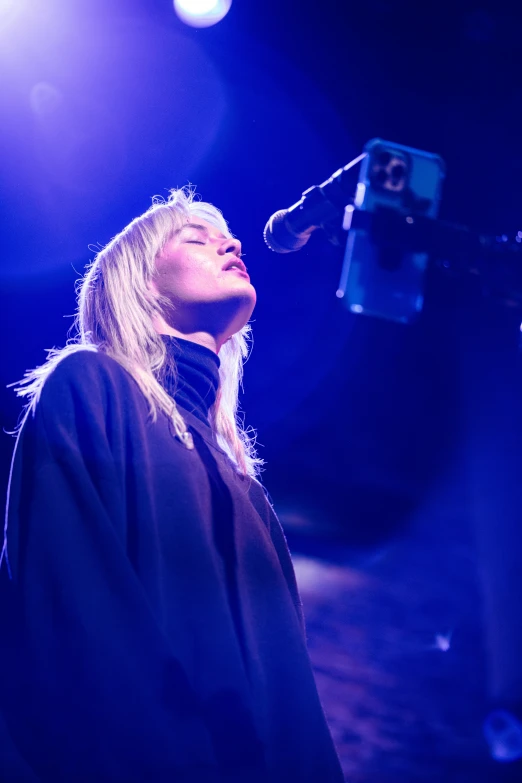 a woman singing into a microphone while standing in front of blue lighting