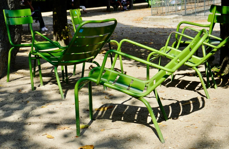 green chairs are sitting in the sand near a tree