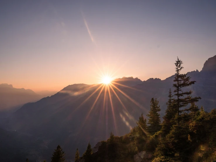 the sun is setting over the mountains above the trees