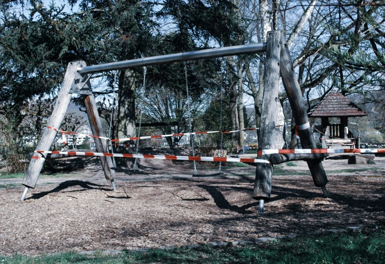 a park area with a broken swing set and an orange and white barricade