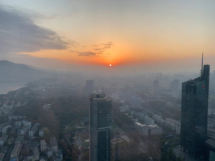 the sun is rising over a large city in a foggy day