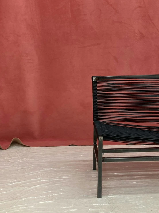 a small black bench sits in front of a pink wall