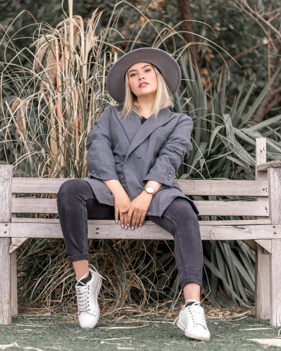 a woman wearing white shoes and a hat sits on a wooden bench