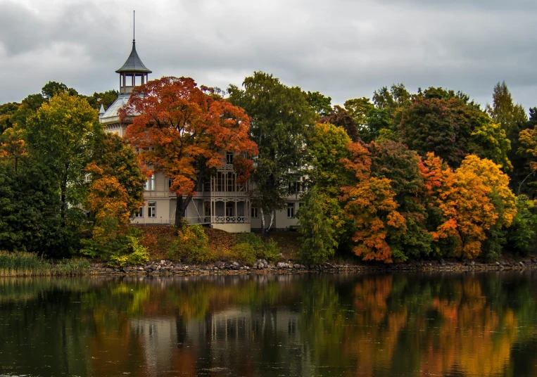 an old house stands on the edge of a lake surrounded by trees