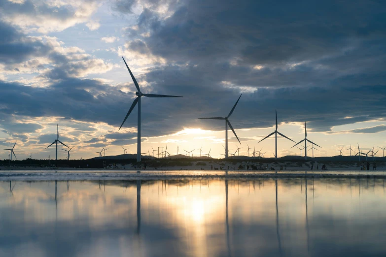 several wind mills in the distance with sun rays behind them