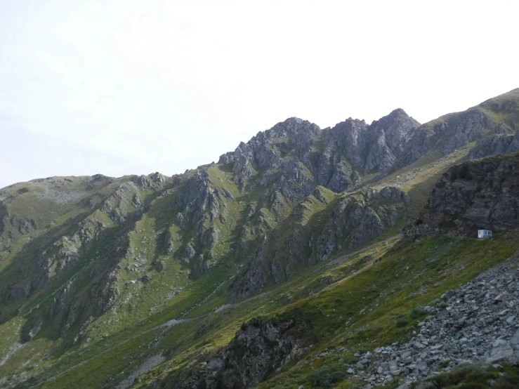 a mountain range covered with rocks, grass and a small white hut