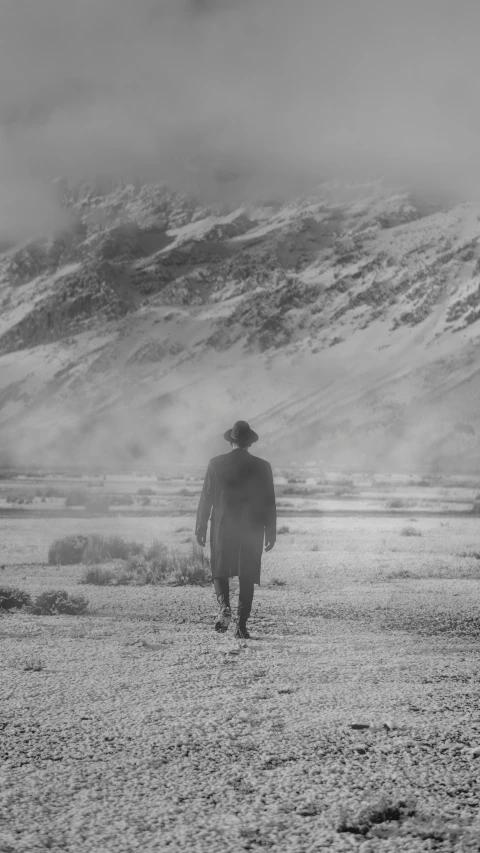 a man in a long coat walking across a desert