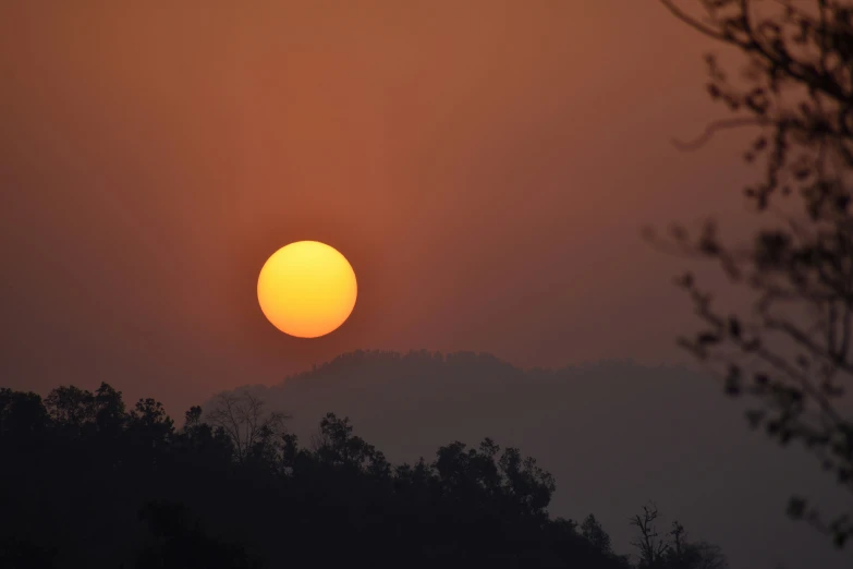 the sun is setting behind the clouds above a forest