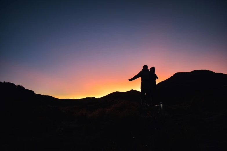 silhouette of two people with arms outstretched on hill top