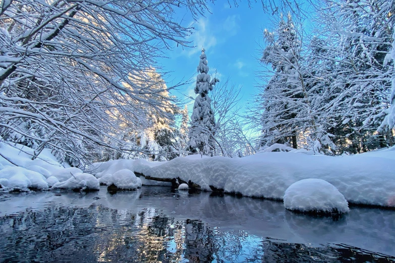 a winter scene with snow on the ground, a creek and trees in the background